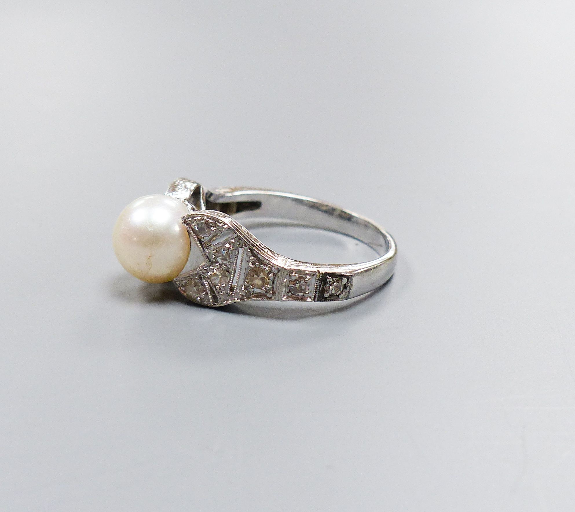 A modern 750 white metal and single stone cultured pearl dress ring, with diamond chip set pierced shoulders, size R/S, gross weight 5.5 grams.